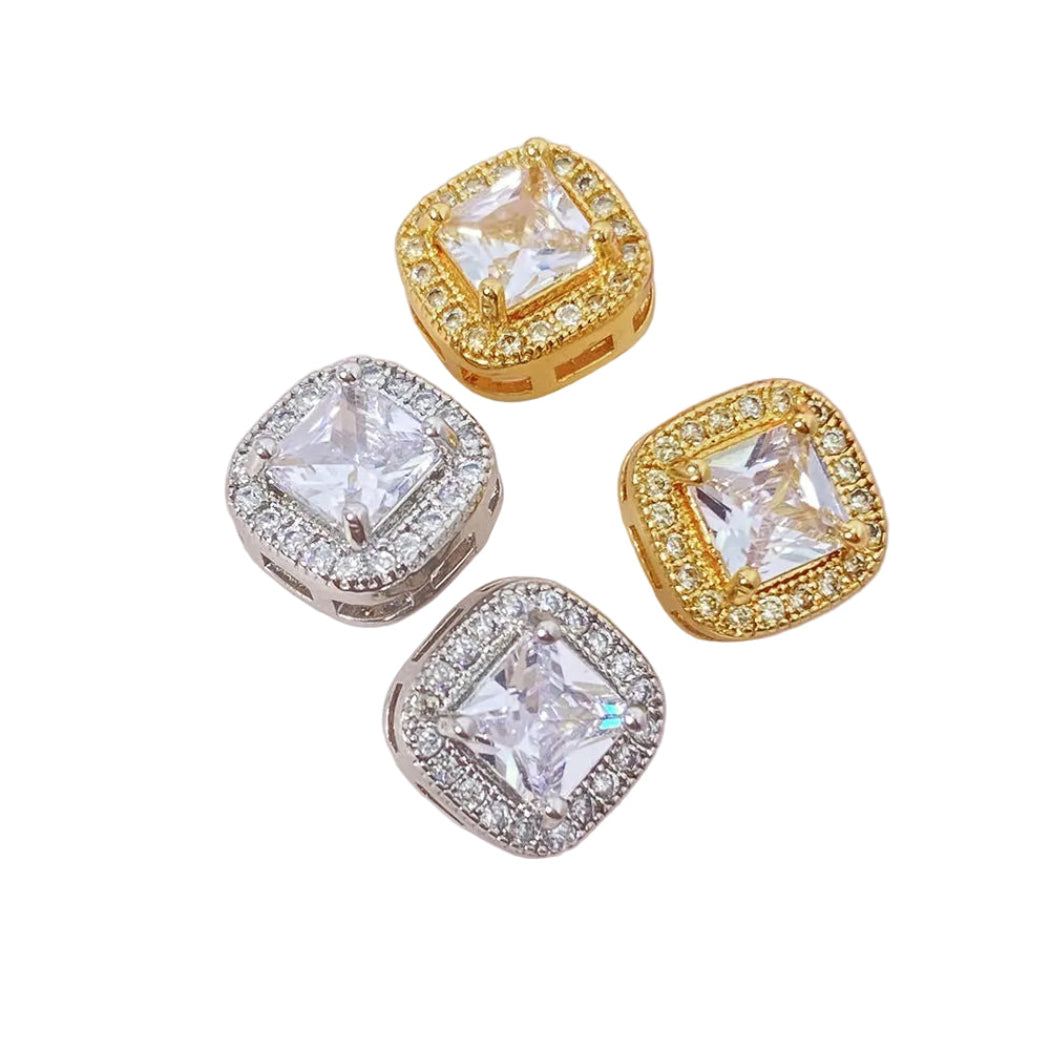 Four diamond-shaped earrings in gold and silver on a pink surface with blurred floral background
