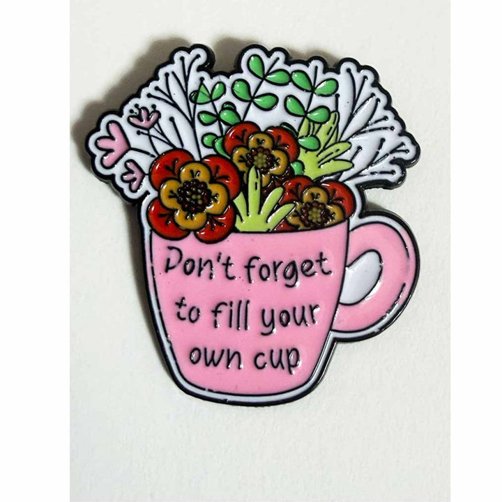Pink enamel teacup pin overflowing with red and gold flowers and greenery, text reading "Don&
