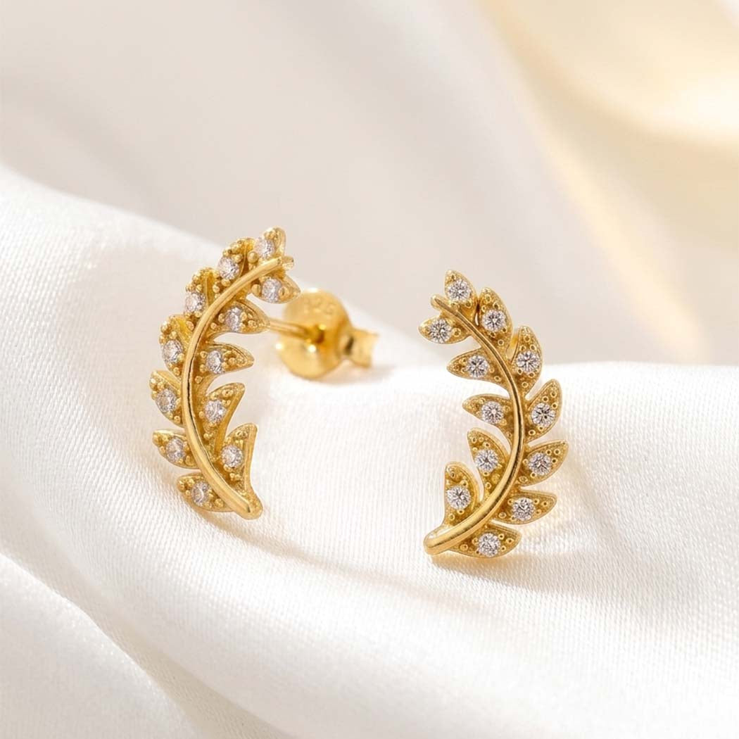 Gold leaf-shaped earrings with embedded stones on a white fabric background