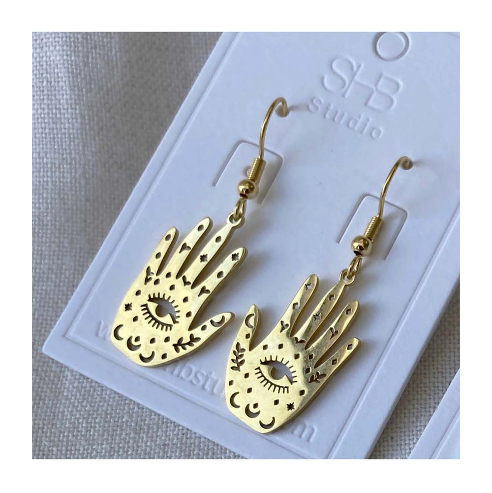 Gold hand-shaped earrings on a white card with 'SHB studio' branding.