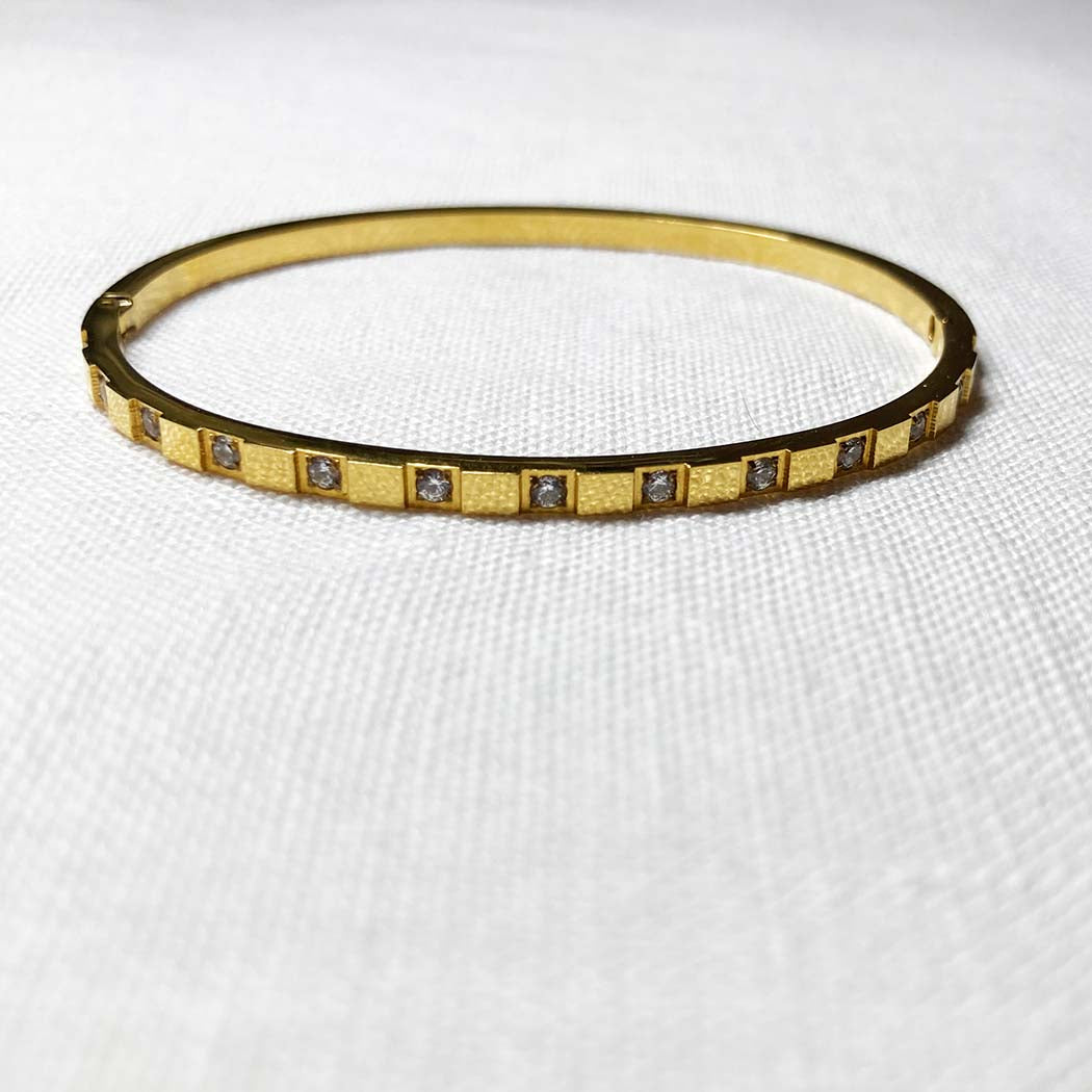 Gold bracelet with embedded zircon on a white fabric background