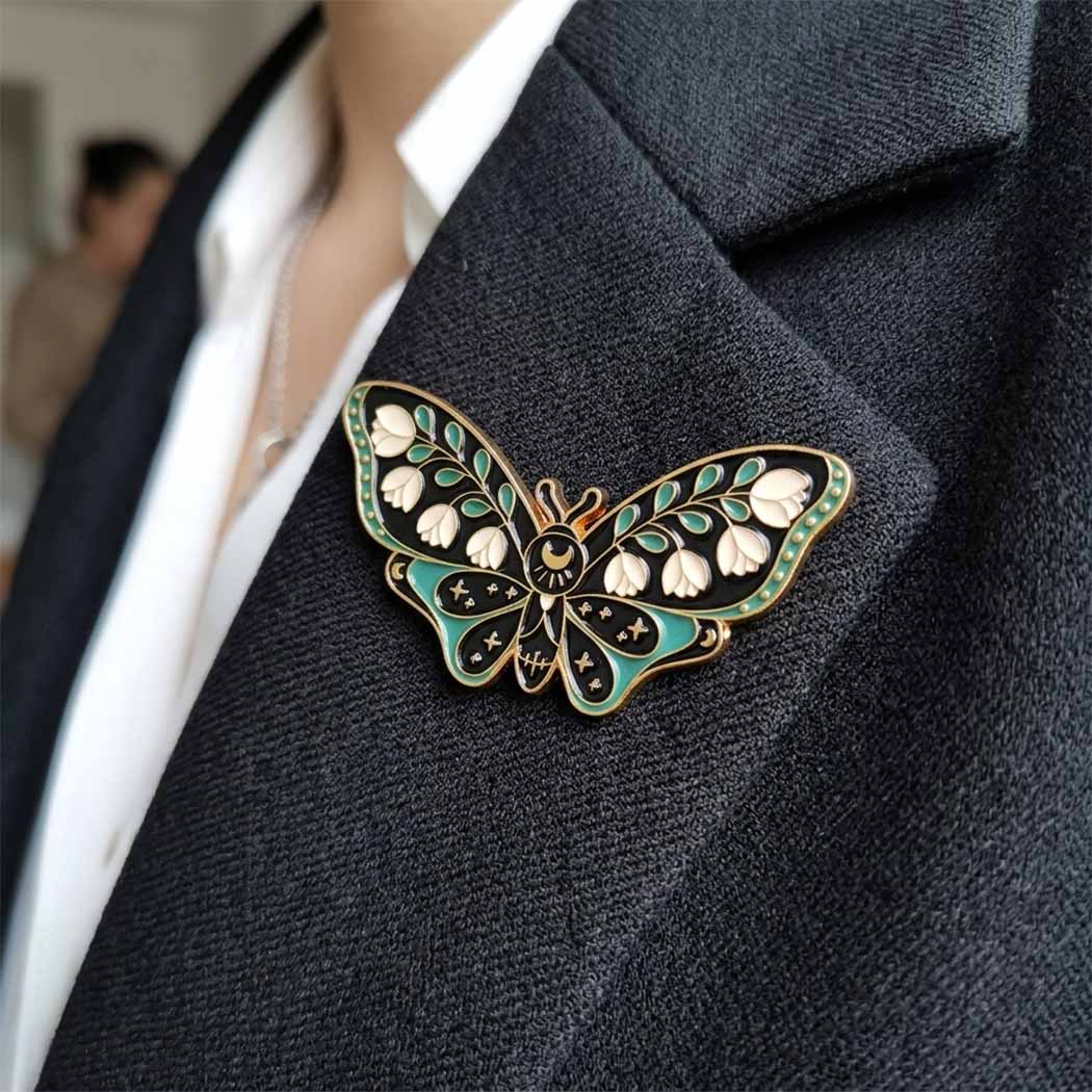 A close-up of a butterfly-shaped lapel pin with green, gold, and white enamel details pinned to a dark gray blazer worn by a person.