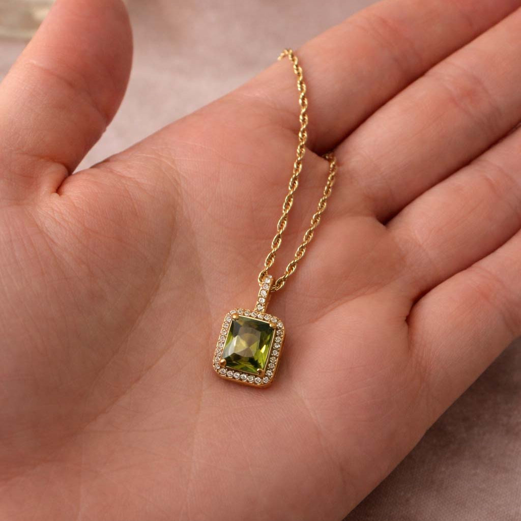 Gold necklace with a green gemstone pendant held in a hand.
