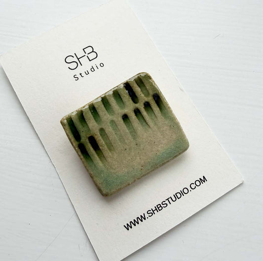 Handmade square ceramic brooch in sage green and cream drip glaze, displayed on an SHB Studio branded card.
