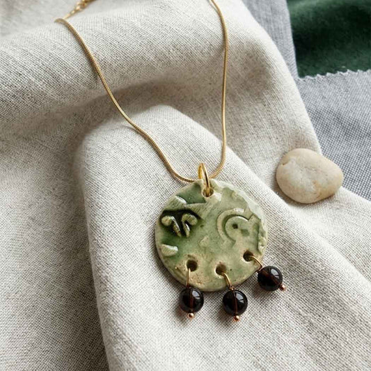 Necklace with a ceramic pendant and beads on a textured fabric background