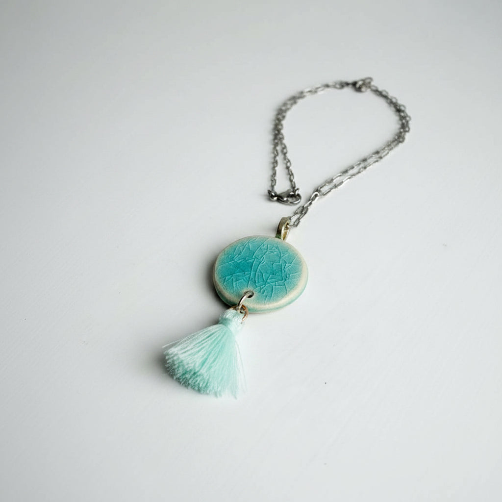 Necklace with a turquoise ceramic pendant and tassel on a white background