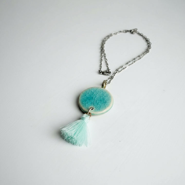 Necklace with a turquoise ceramic pendant and tassel on a white background