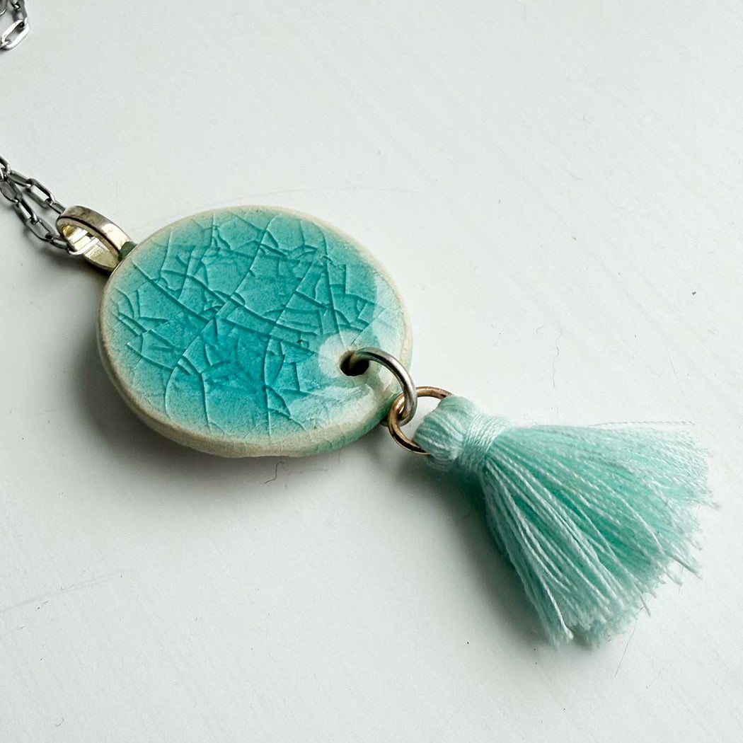 Turquoise ceramic pendant with tassel on a white background