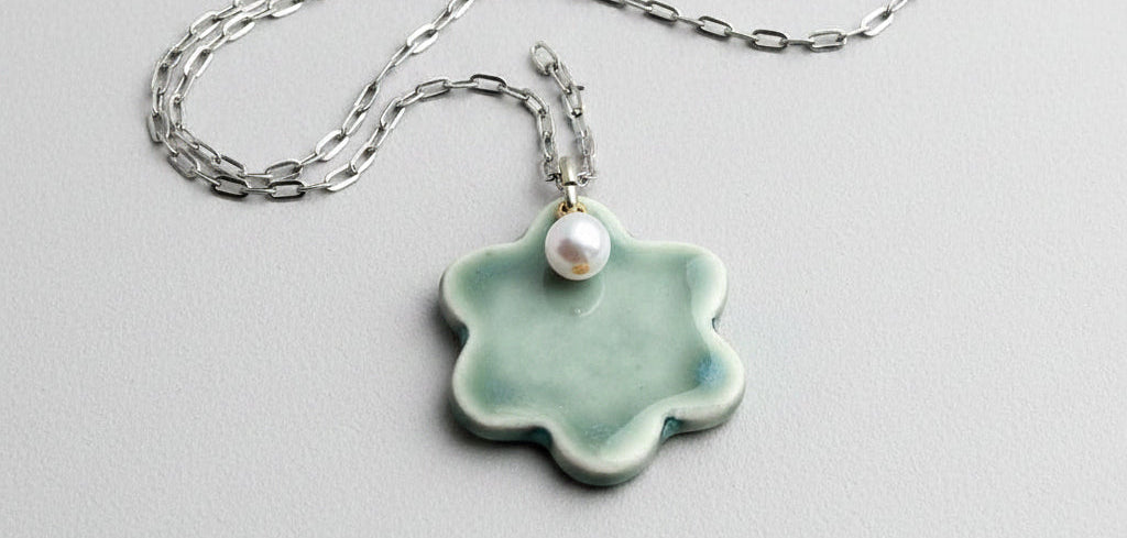 Flower-shaped pendant with a pearl on a chain held in a hand.