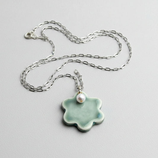 Flower-shaped pendant with a pearl on a chain held in a hand.