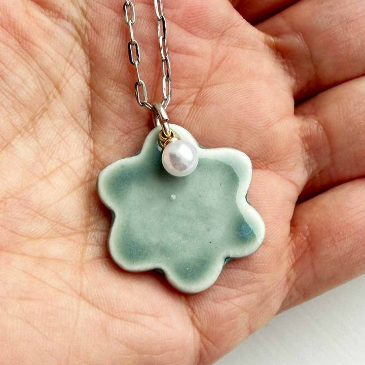 Necklace with a green ceramic pendant and pearl held in a hand.