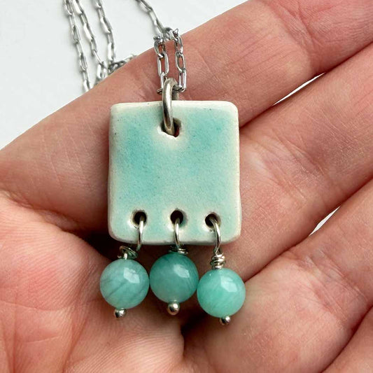Necklace with a square pendant and three green beads held in a hand.
