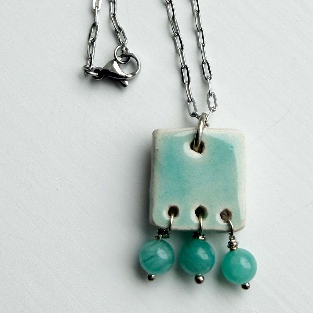 Necklace with a square pendant and three hanging beads on a light gray background