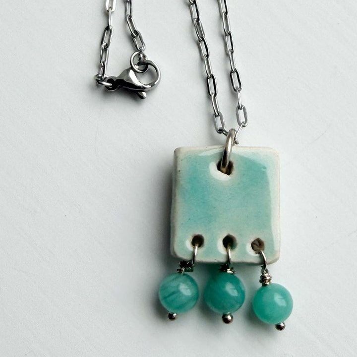 Necklace with a square pendant and three hanging beads on a light gray background