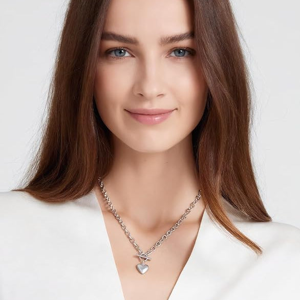 Woman wearing a silver necklace with a heart pendant on a white background