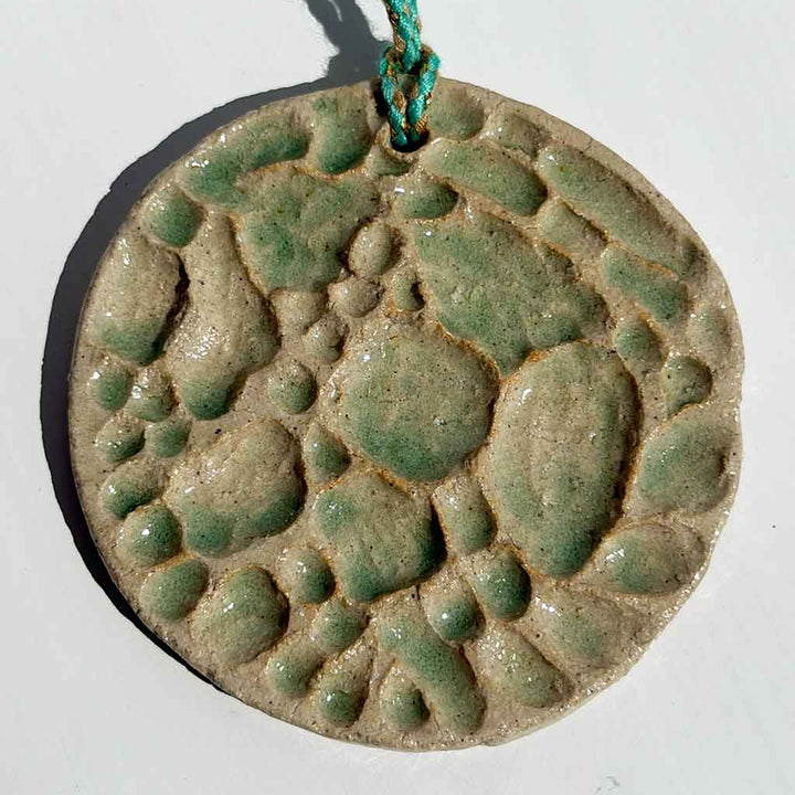Green ceramic pendant with textured surface on a white background