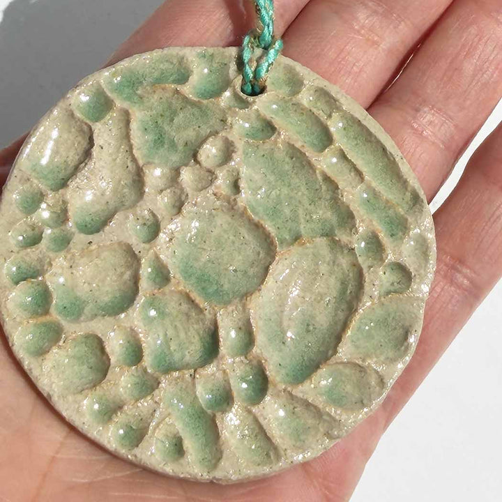 Green textured circular pendant held in a hand against a neutral background