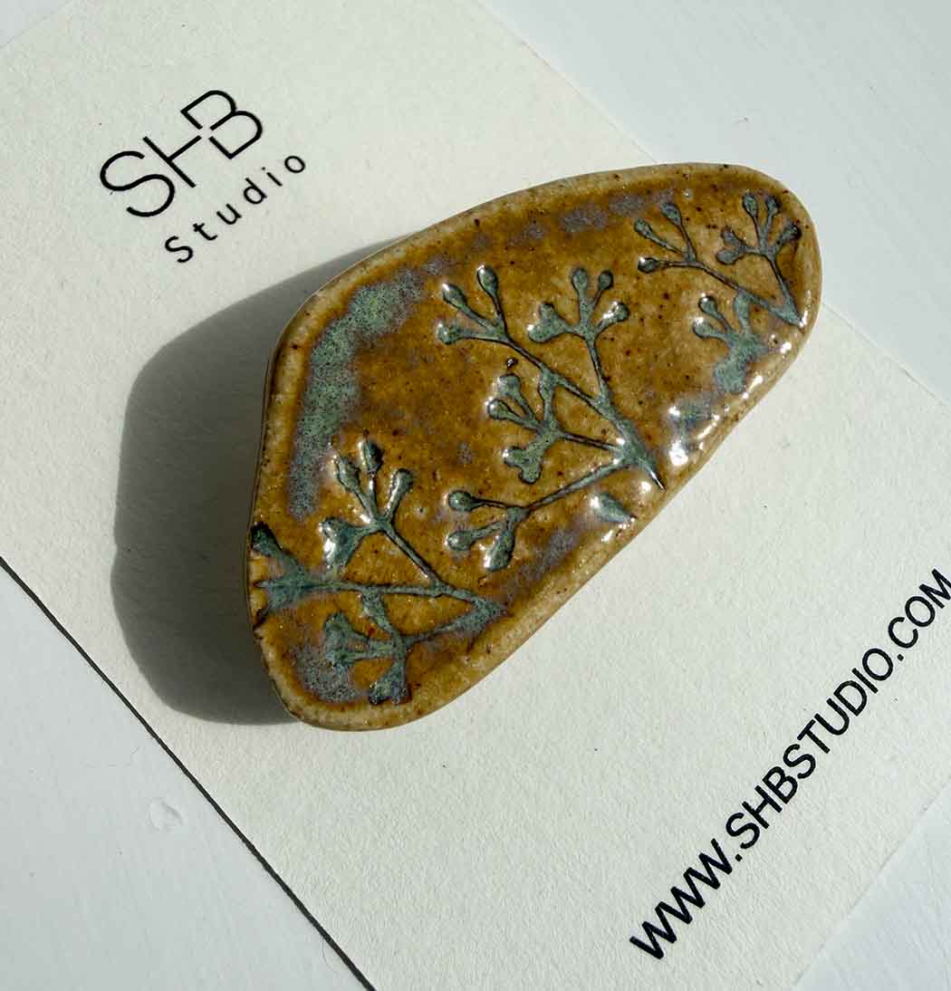 brooch with floral pattern on a white card with SHB Studio branding.
