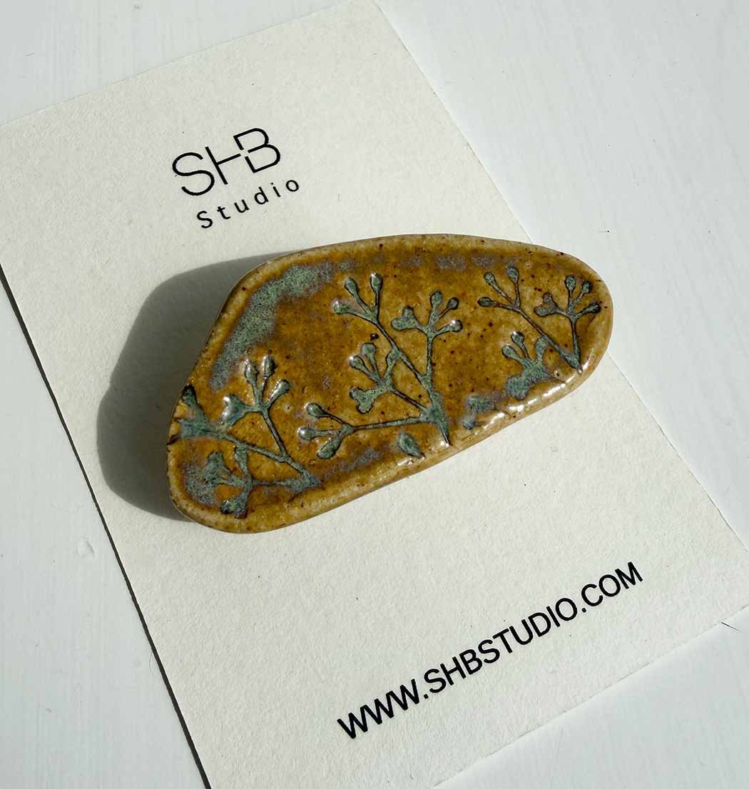 Ceramic brooch with floral design on a white card with SHB Studio branding