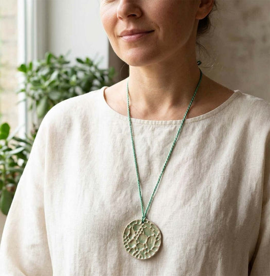 Woman wearing a necklace with a large ceramic handmade light green pendant indoors