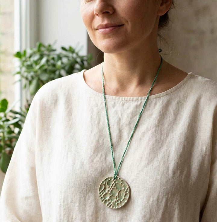 Woman wearing a necklace with a large ceramic handmade light green pendant indoors