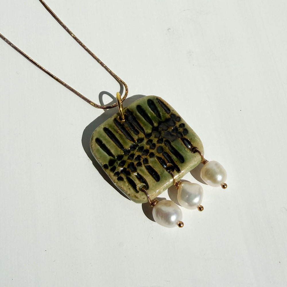 Necklace with a green ceramic pendant and pearl beads on a white background