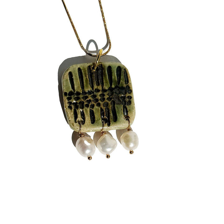 Necklace with a square pendant featuring black patterns and three pearl-like beads on a white background