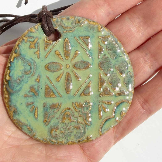 Hand holding a ceramic pendant with intricate patterns