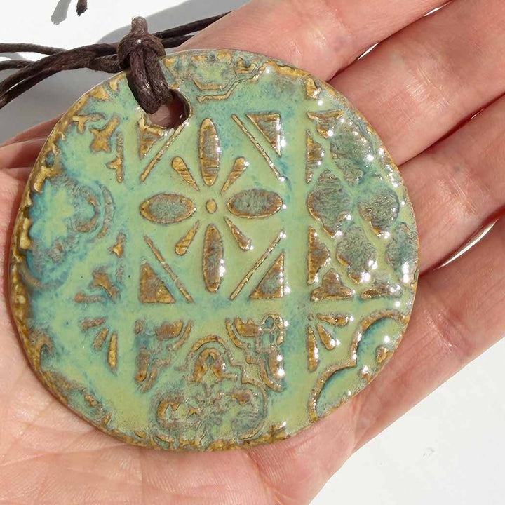 Hand holding a ceramic pendant with intricate patterns