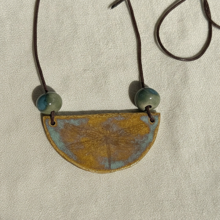 ceramic Necklace with a half-circle pendant and green beads  dragonfly gold lustre on a white background