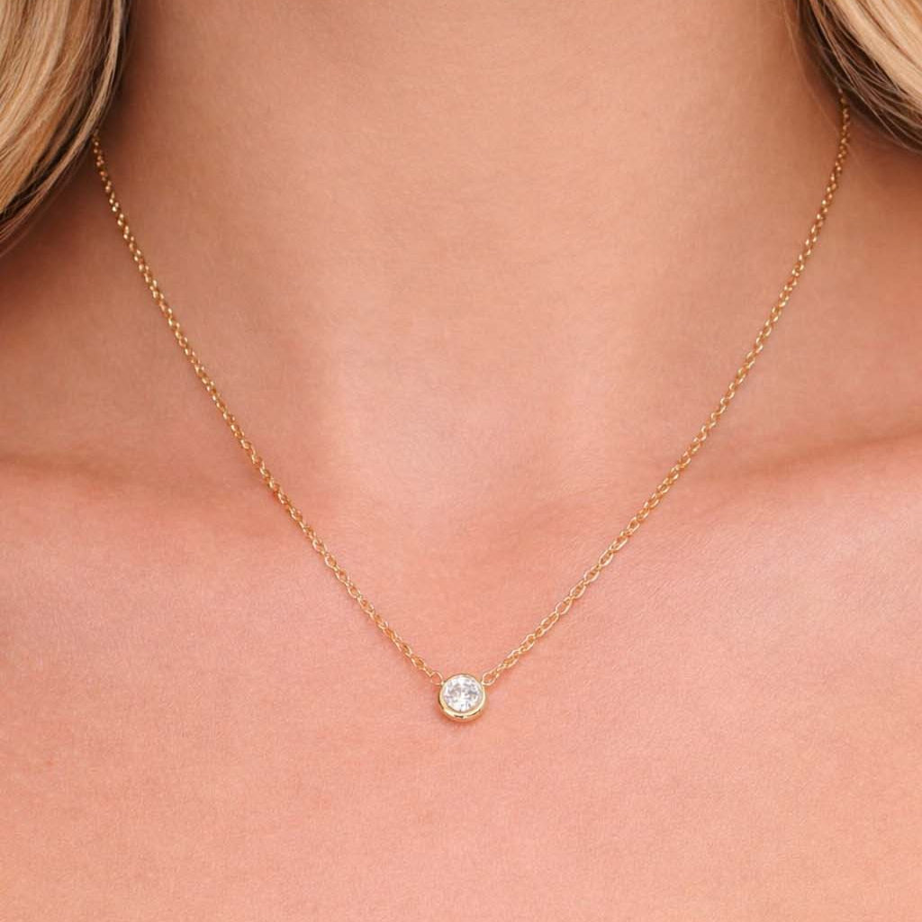 Gold necklace with a small round pendant on a person's neck