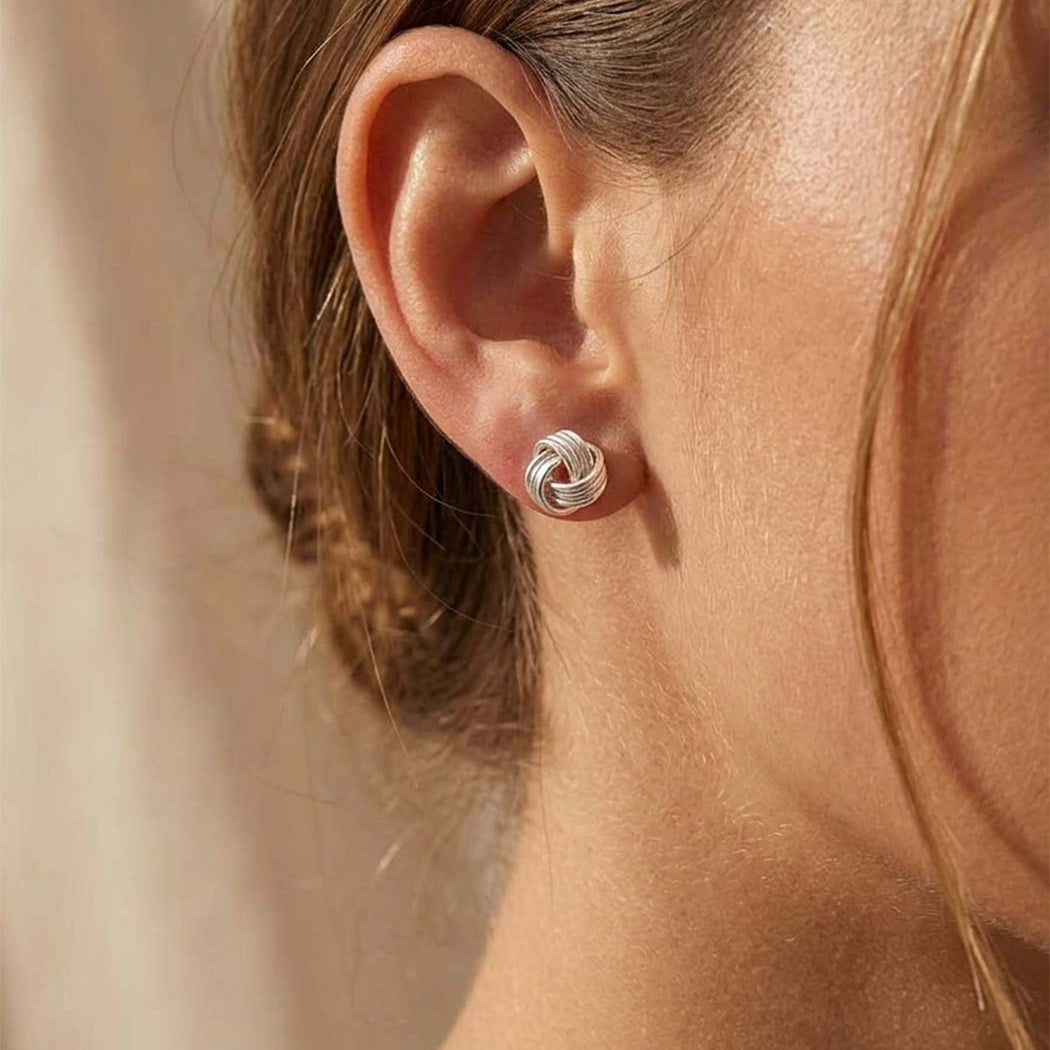 Close-up of a person wearing a silver knot earring against a neutral background