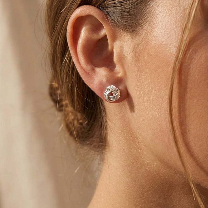 Close-up of a person wearing a silver knot earring against a neutral background