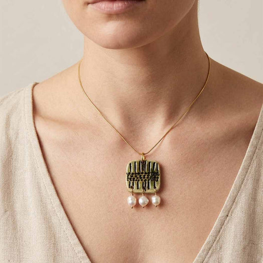 Necklace with a pendant featuring three pearls worn by a person.