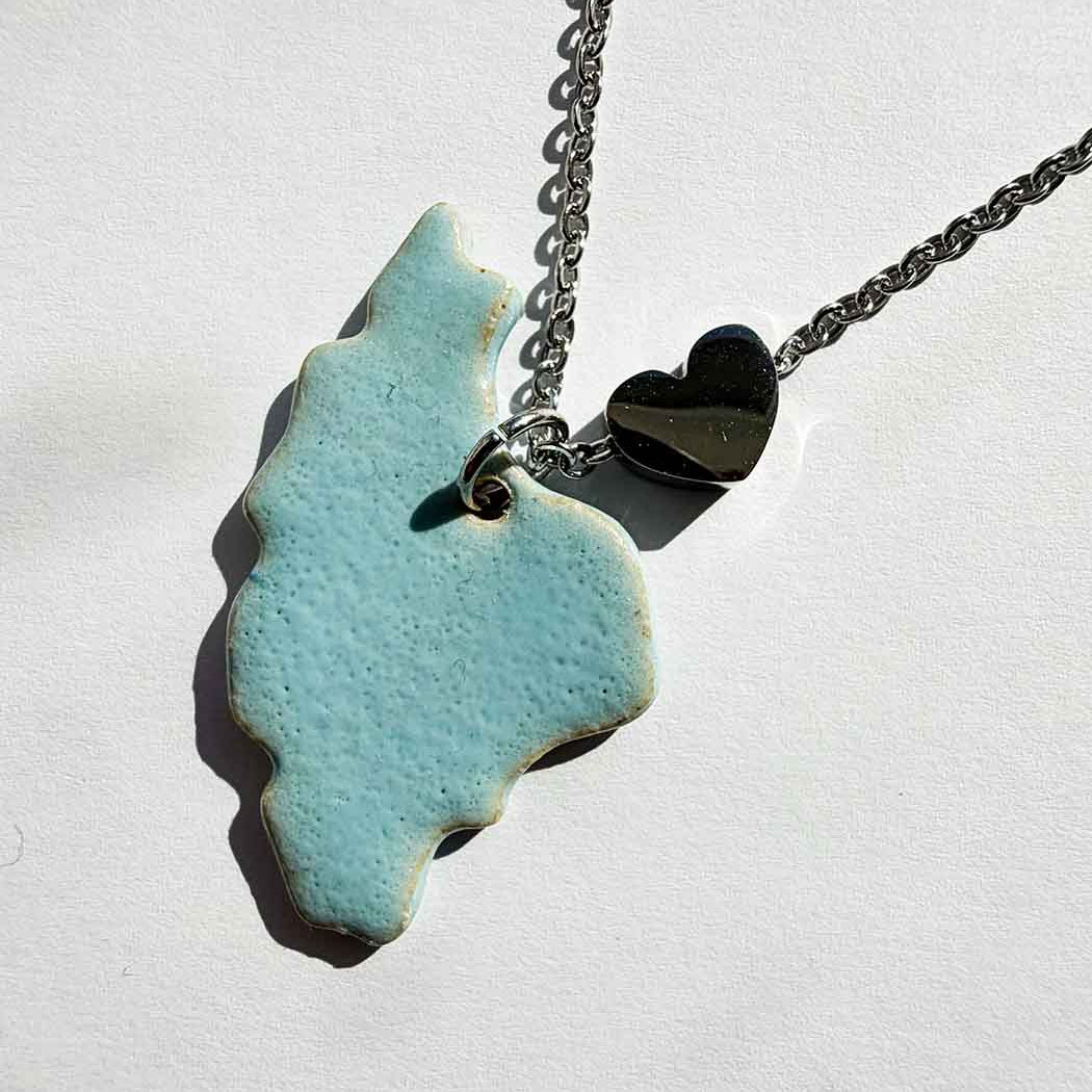 Necklace with a blue ceramic handmade iran map pendant littel heart silver colour near iran map on a white background