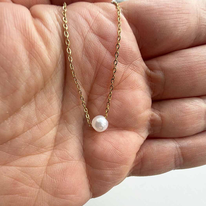 Gold necklace with a single pearl pendant held in a hand.