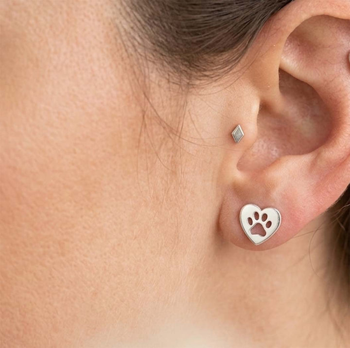 Silver heart-shaped earring with paw print worn by a person
