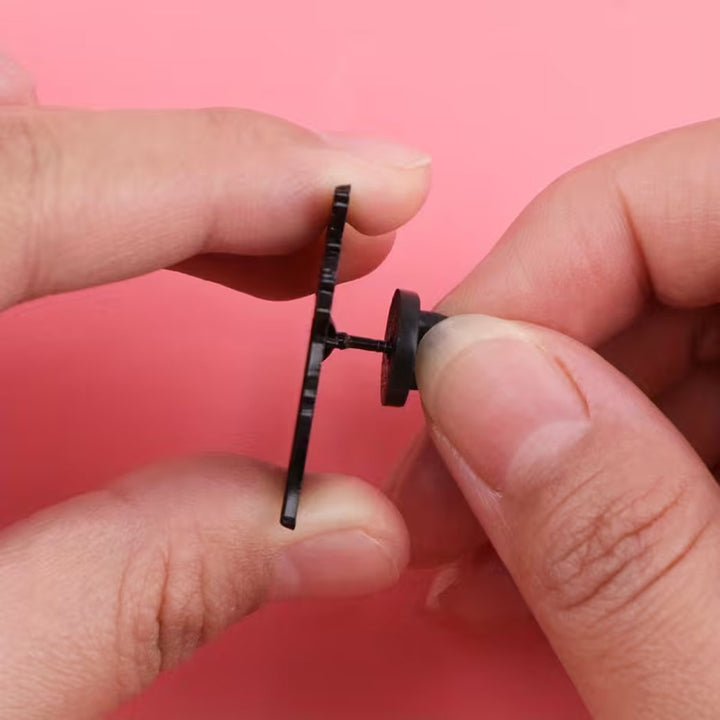 Close-up of hands holding a small black pin badge against a white background