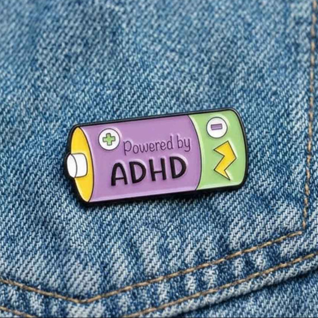 A battery-shaped enamel pin with the text &