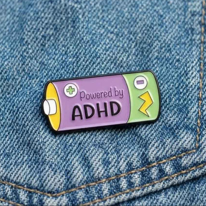 A battery-shaped enamel pin with the text &
