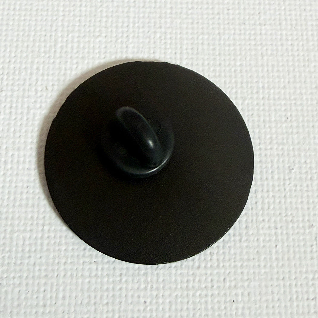 A small black circular back side of pin badge shown on a textured white background.