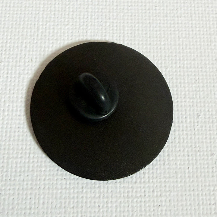 A small black circular back side of pin badge shown on a textured white background.