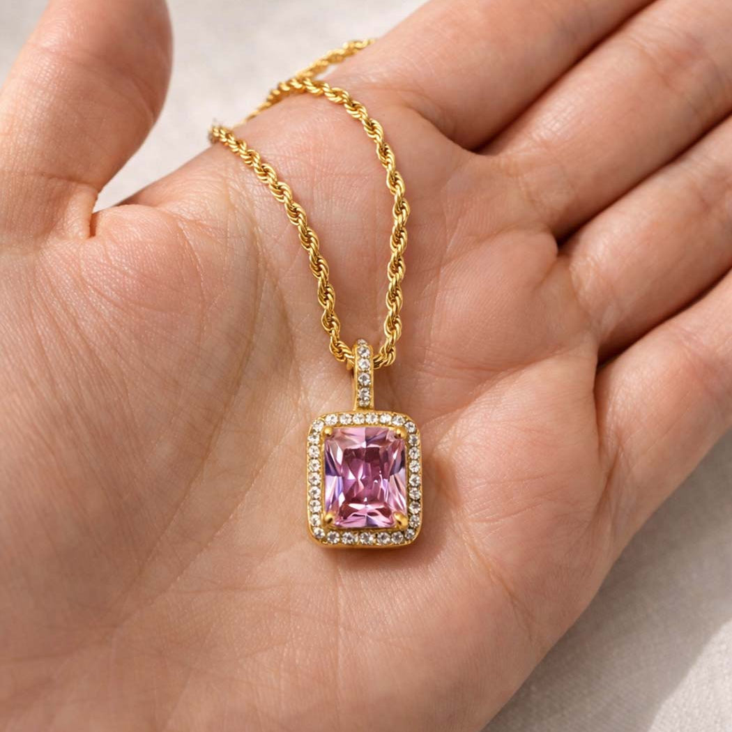 Gold necklace with a pink gemstone pendant held in a hand.