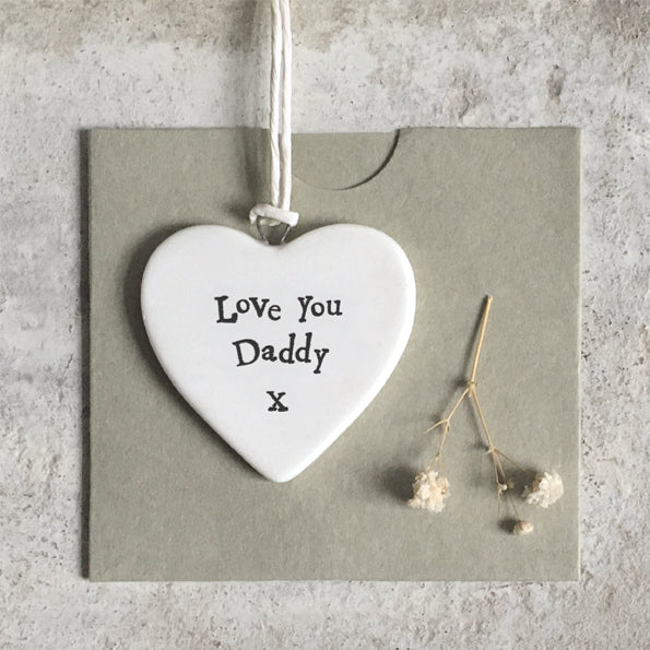 Heart-shaped ceramic tag with 'Love You Daddy X' text on a gray card with dried flowers.