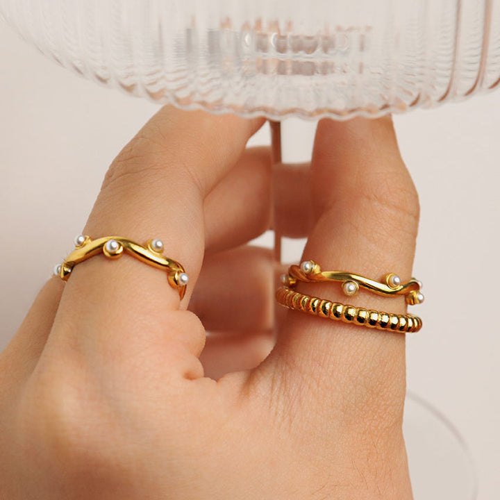 Gold rings with pearl accents on a hand against a neutral background
