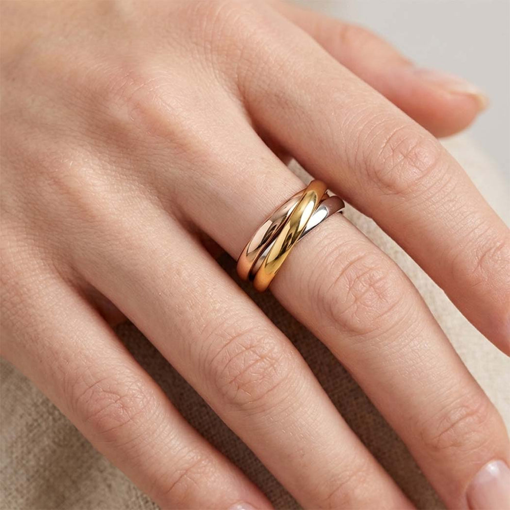 A close-up of a hand wearing a twisted Three-tone ring with one gold band and one rose gold and silver band.