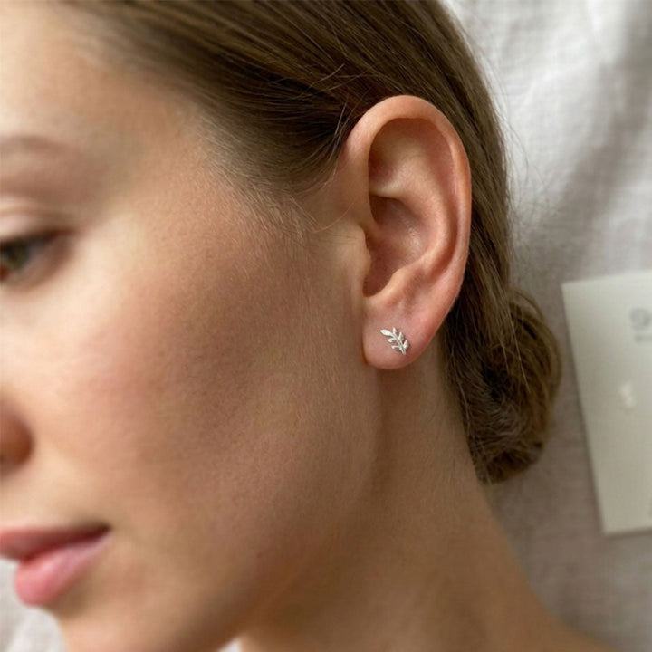 Close-up of a person wearing a silver earring with a clear gemstone, against a neutral background.