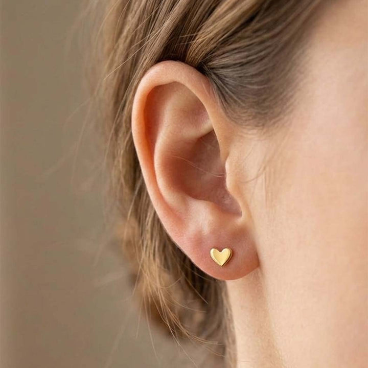 Gold heart-shaped earring worn by a person with a neutral background