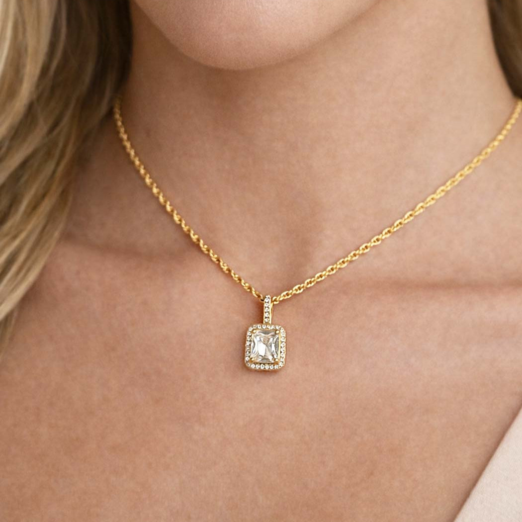 Gold necklace with a white zirconia square pendant on a person's neck.