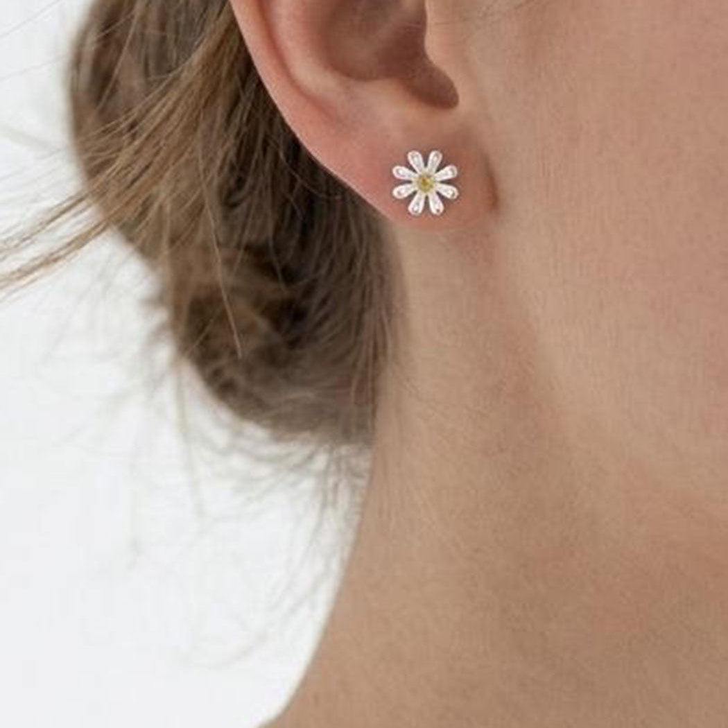 Close-up of an ear wearing a daisy-shaped earring on a plain background